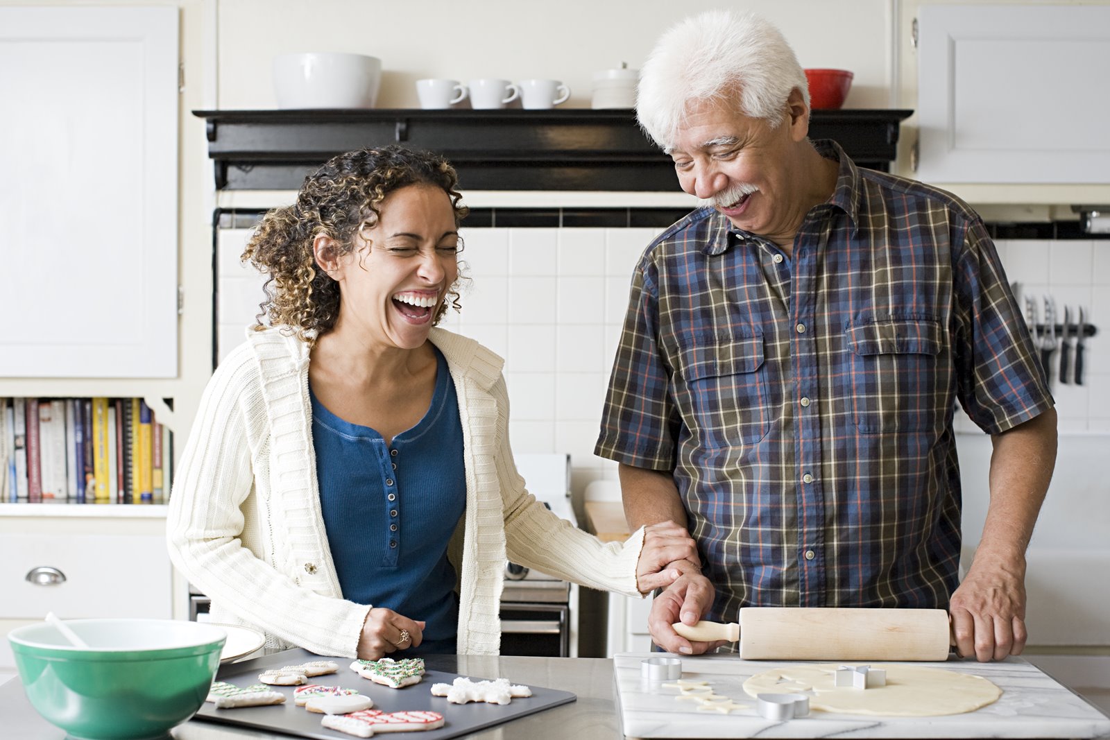 Two elderly people smiling as they bake a cake together