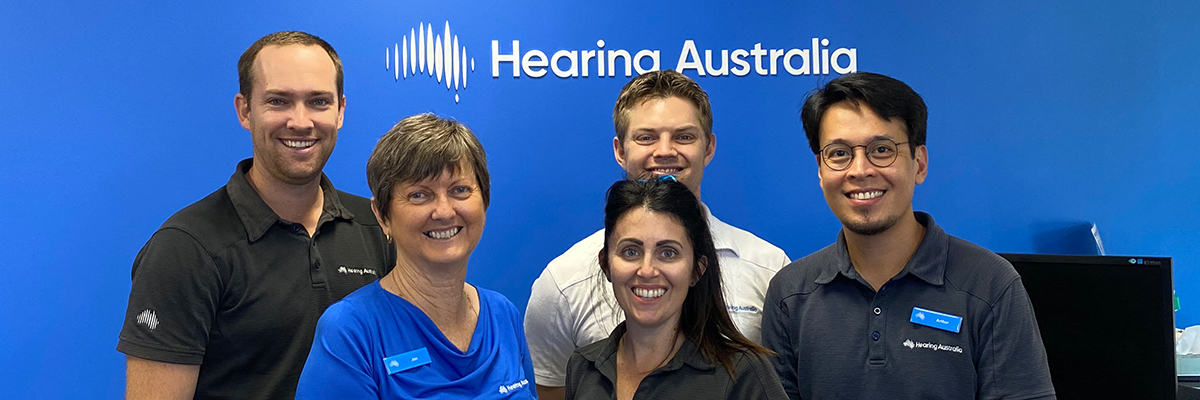Five Hearing Australia team members smiling warmly and friendly at a Hearing Australia centre