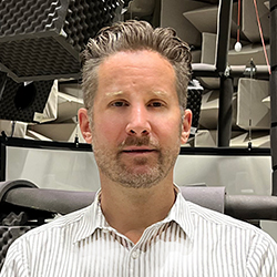 Matt, Research Audiologist at NAL, standing with NAL background